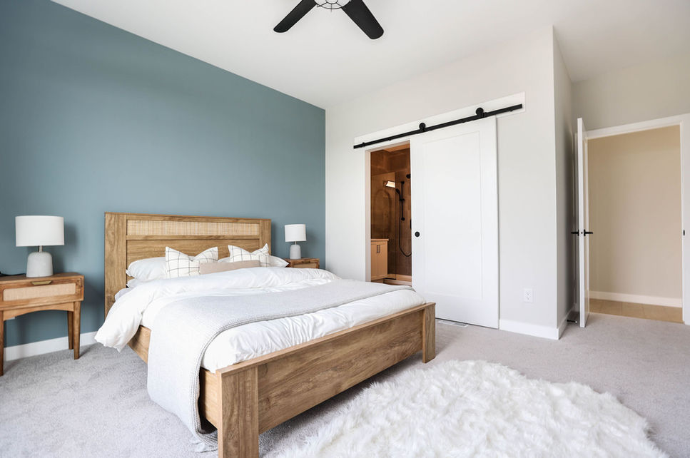 Primary bedroom at 3 Benjamin Boulevard with wood bed frame, blue accent wall, barn door ensuite entry, and carpeted flooring.