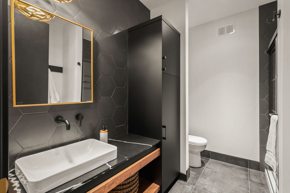Bathroom at 6 Avonlynn Court with black hex tile feature wall, vessel sink, gold-framed mirror, and wood vanity detail.