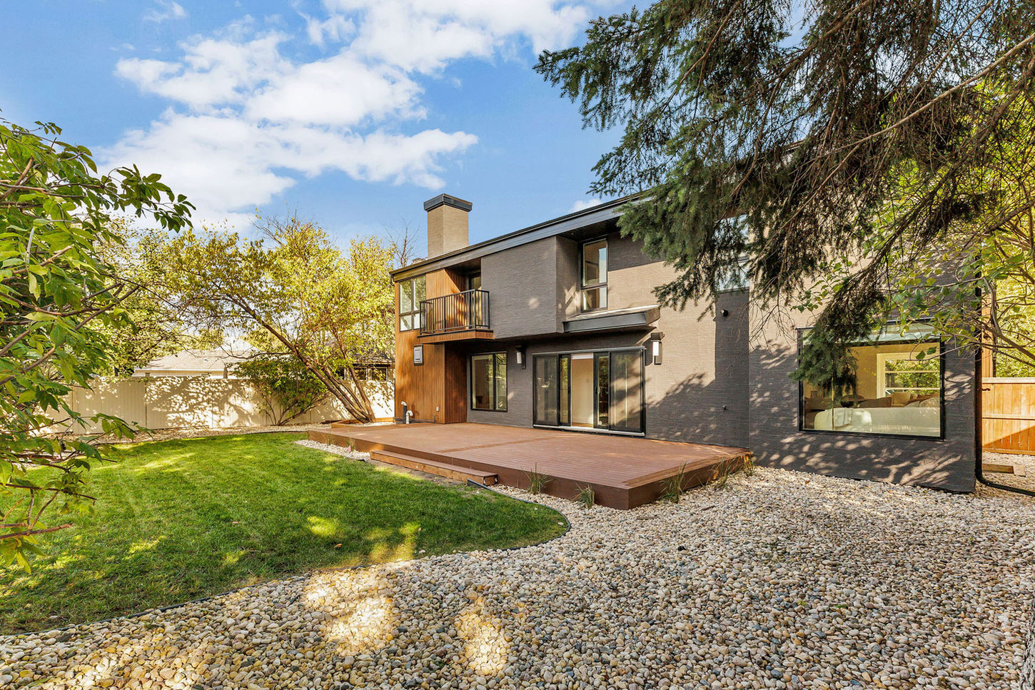 Rear exterior of 67 Dunbar Crescent with large wood deck, second-floor balcony, and landscaped backyard.