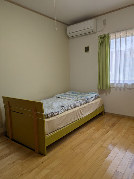 シングルベッドが置かれた部屋。空調、カーテン、フローリング。共同生活援助、社会福祉法人 竹の里。