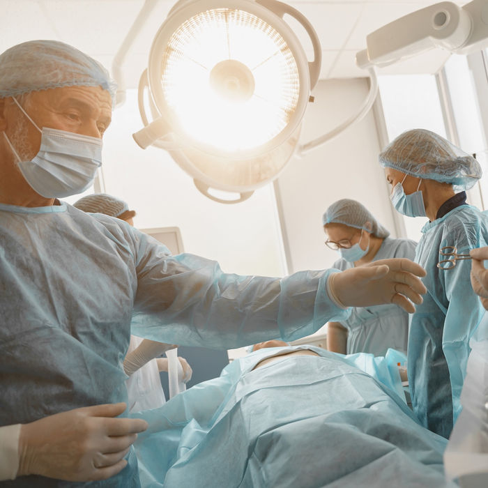 手術室で手術をする医師と看護師、手術器具、照明、患者の姿が見える。