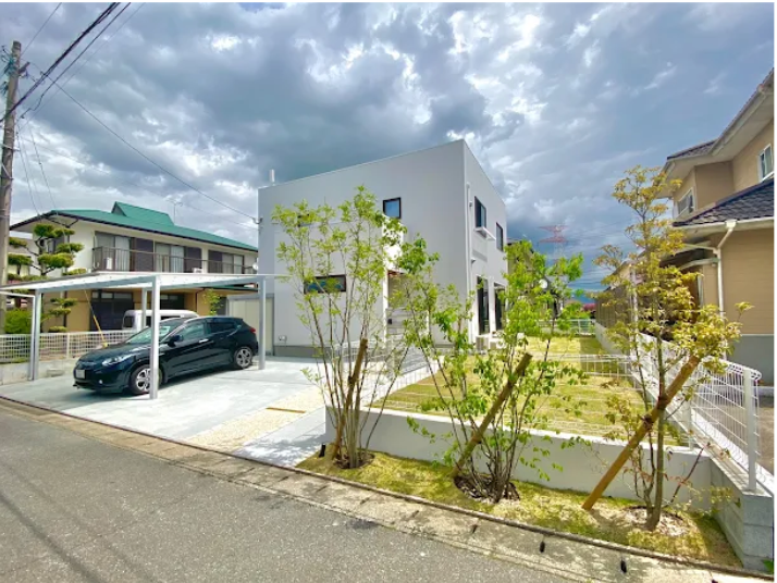 白い家と車、駐車場。Y・Cエクステリア、美しい庭。曇り空、住宅街の風景。