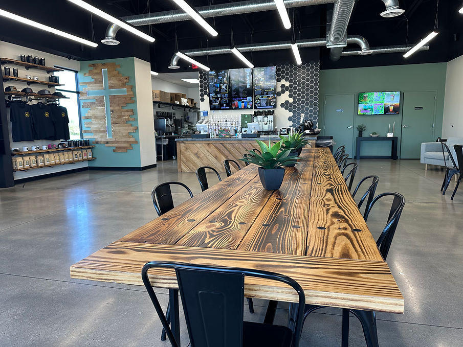Long communal wood table at the KINGDOM Coffee cafe in St Joseph, MO, with bagged coffee for sale on the back wall