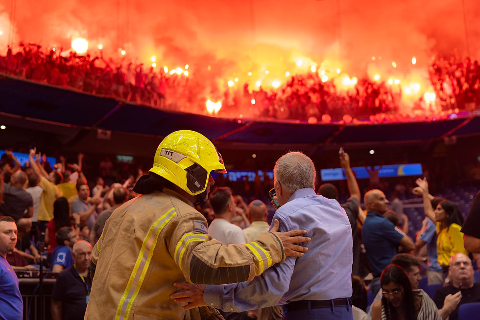 שמעון מזרחי, יו״ר מכבי תל אביב בכדורסל, וכבאי ניצבים מול יציע אפוף עשן ואבוקות שהציתו אוהדי הפועל תל אביב בהיכל מנורה מבטחים במהלך המשחק הראשון בסדרת הגמר.