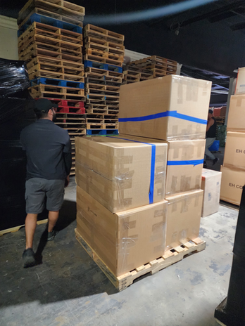 Man walks past stacked cardboard boxes and tall wooden pallets in warehouse.