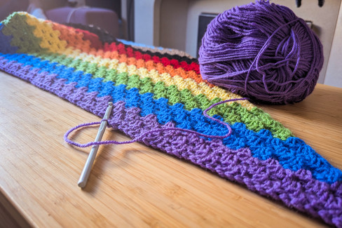 a progress pride flag crochet shall partially finished, with the crochet hook and a ball of yarn attached