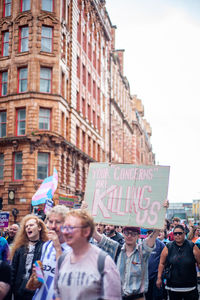 a protester in the middle of a crowd holds up a sign that says 'your "concerns" are killing us' at Trans Pride Manchester 2023