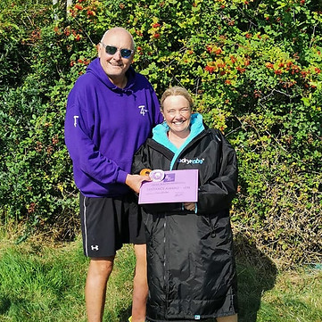 Paul handing out a certificate to a river swimmer on a sunny day stood in front of a bush
