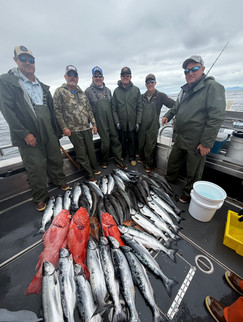 Group of guests posing with their catch in front of an Alaska fishing lodge after a successful day on the water.