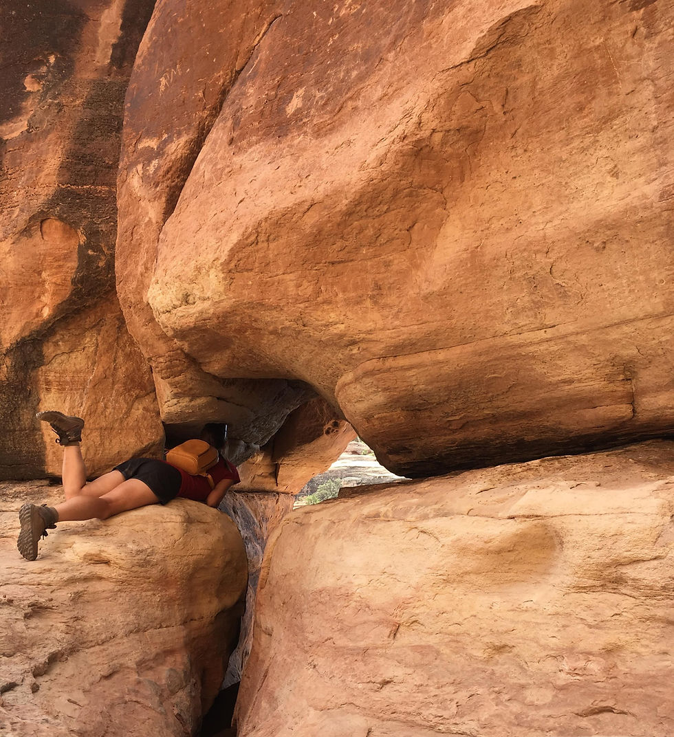 woman lying on orange rock peering through a gap in the rocks