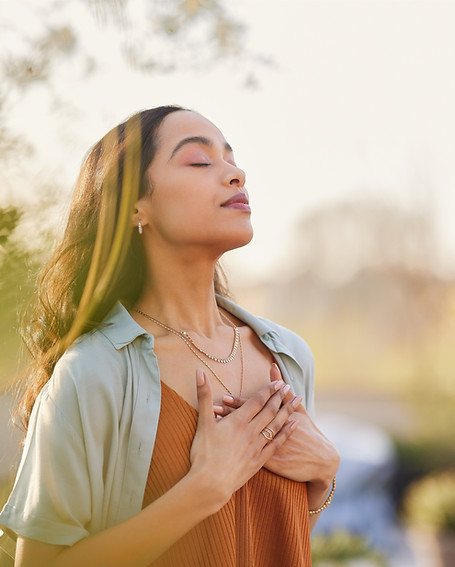 Young latin woman with hand on chest breathing in fresh air in a beautiful garden during s