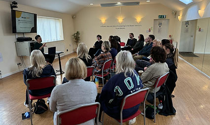 A large group seated in a room listening to a lead speaker