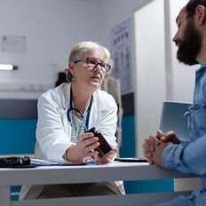 Médica explicando medicación a paciente masculino barbudo en una consulta.