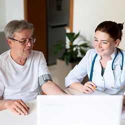 Doctora midiendo presión arterial a hombre mayor con laptop en casa.