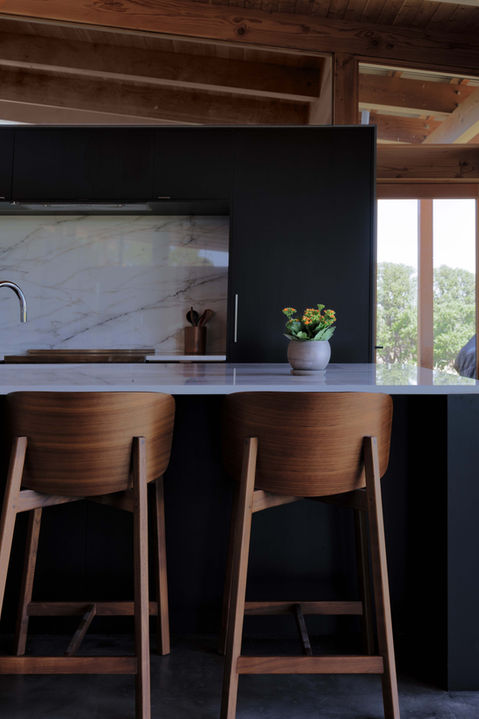 A modern kitchen design with carved walnut counter stools and modern black cabinetry.