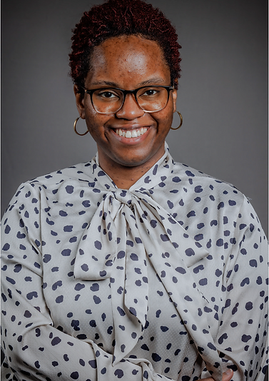 A black woman in a polka-dot professional blouse in front of a grey background.