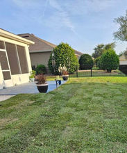 Manicured green backyard lawn, screened patio, potted plants, and trimmed bushes.