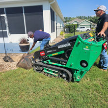Two men operate Toro Dingo TX 1000 mini skid steer for landscaping.