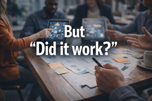Team meeting around a wooden table reviewing marketing reports while a woman points at a tablet displaying charts. A Black man sits at the head of the table observing the discussion. Overlaid text reads, “But ‘Did it work?’” indicating a focus on marketing performance and results.