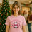 Thumbnail: Woman wearing pink shirt with 'Namasleigh' Santa Claus design in front of tree.