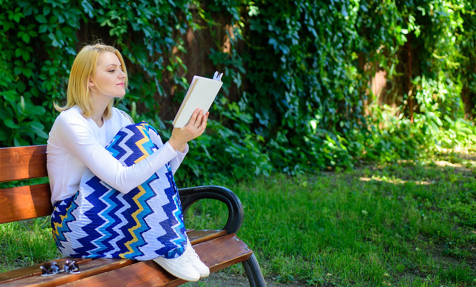 A young woman sits on a bench reading a book.