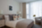 Contemporary bedroom with upholstered bed, tailored curtains, statement cushions and floor-to-ceiling glazing in a luxury Waterloo apartment designed by Studio Clementine.