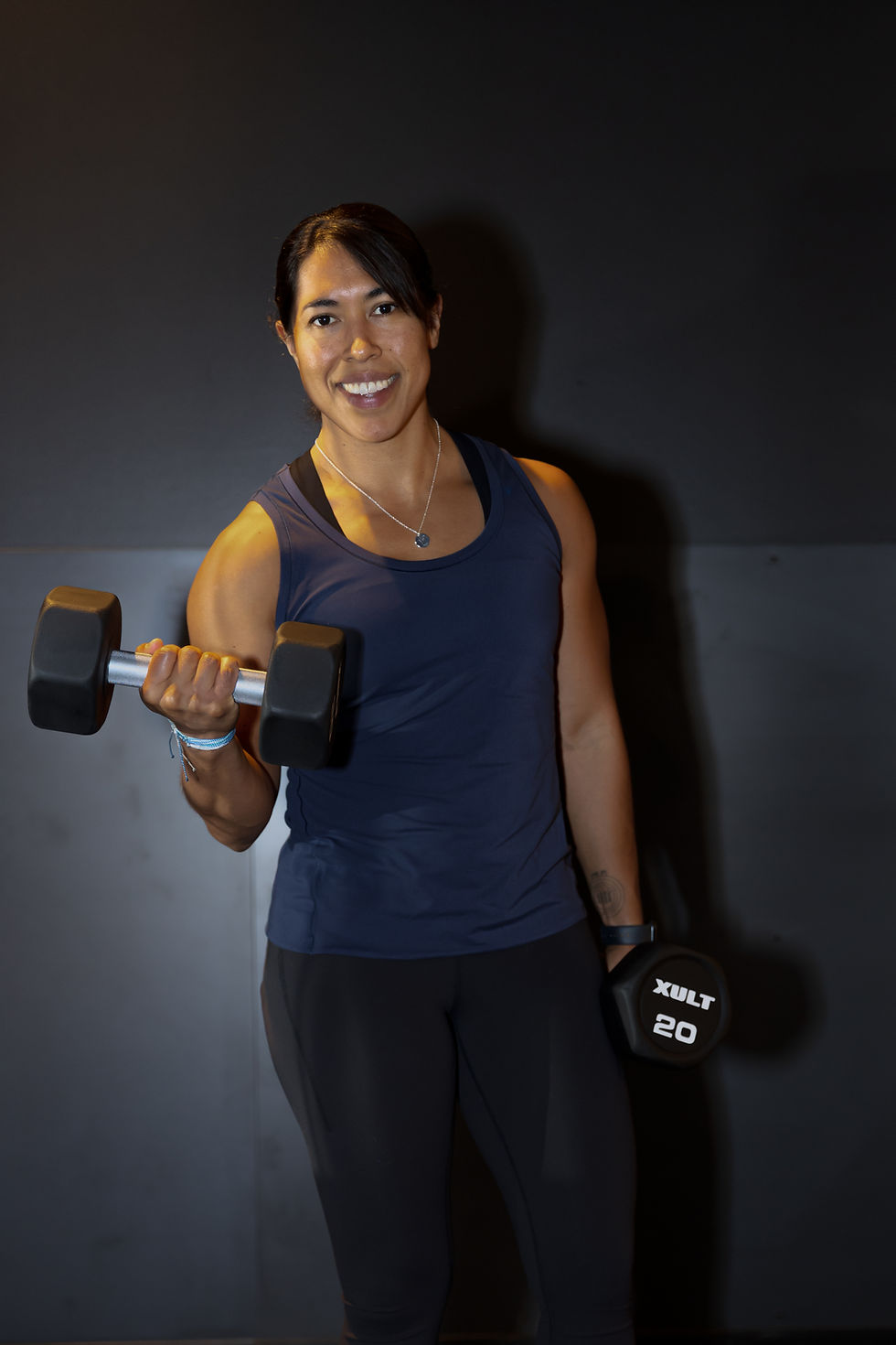 A woman smiling while holding 20-pound dumbbells in a gym.