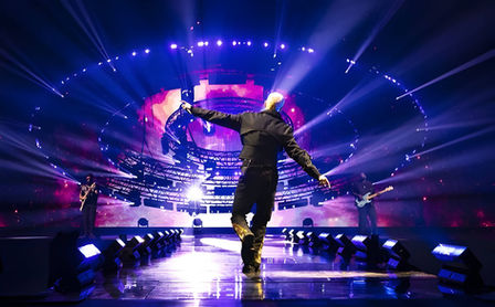 M Pokora en pleine action, dansant sur une scène éclairée par des lumières puissantes et des écrans LED animés, renforçant l'énergie et le dynamisme de sa performance.