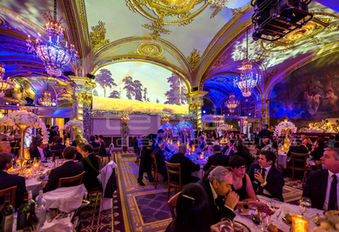 Salle de réception remplie d’invités, éclairée par des projections de paysages pittoresques et des lumières bleues qui enveloppent la pièce dans une ambiance mystique et royale.
