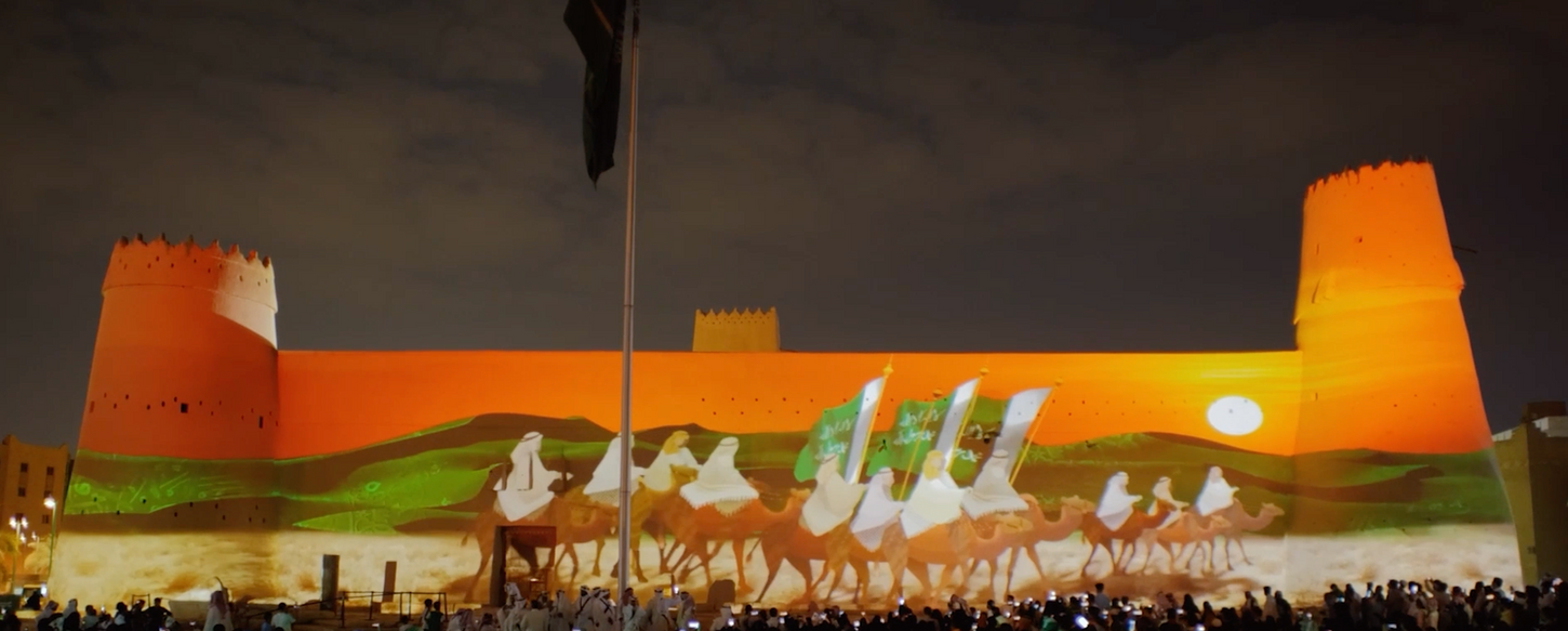 La façade du Fort Masmak est illuminée par des projections animées de cavaliers traversant un paysage désertique, racontant une partie de l'histoire du royaume saoudien. Ce spectacle visuel attire une foule de spectateurs venus célébrer le National Day.
