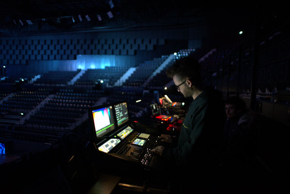 Technicien lumière et son travaillant dans une régie au sein d'une salle de spectacle vide, entouré de consoles et d'écrans, en préparation d'un événement à venir.
