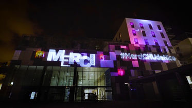 Une autre vue de la façade du CHU avec le mot "Merci" projeté en grand, accompagné d'images de professionnels de santé. Les projections rendent hommage aux héros anonymes qui ont contribué à la gestion de la crise du Covid-19.