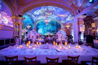 Grande table de banquet ornée de décorations élégantes et de bougies, sous un plafond illuminé par des projections de nuages et de ciels, créant une ambiance magique et intime pour les invités.