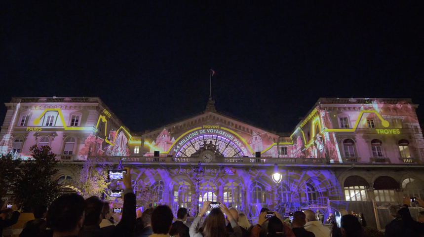 Scène illuminée de projections complexes sur la façade d'une gare, mêlant des images de train et d'éléments historiques pour célébrer son héritage.
