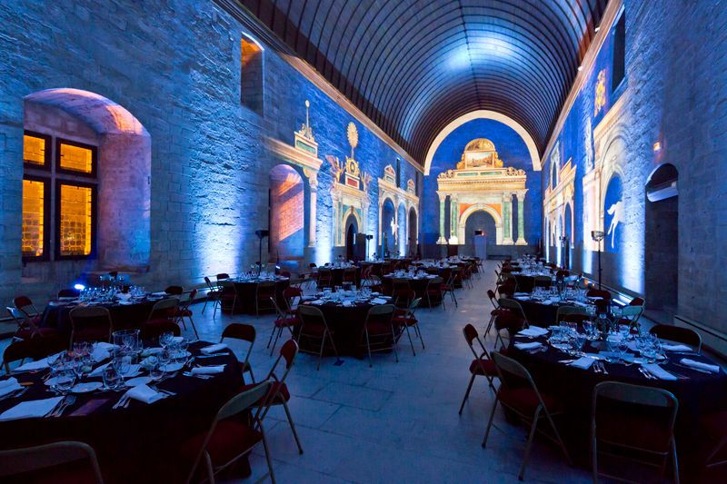 Ambiance feutrée avec éclairage bleu et arches projetées, transformant l’espace du Grand Tinel en une salle de banquet historique pour événements privés.
