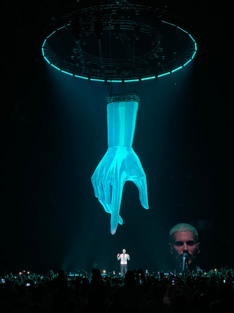 Une main géante en projection 3D surplombe la scène pendant une performance émotive de M Pokora, créant une atmosphère unique et onirique grâce aux décors numériques élaborés par Studio Énorme.
