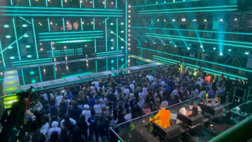 La scène de l’émission est baignée dans des lumières vertes et bleues, tandis que le public observe attentivement les performances. Les contenus visuels projetés sur les écrans LED synchronisent parfaitement avec le rythme des prestations.