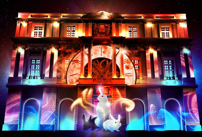 La façade d’un bâtiment historique est illuminée par des projections de rouages et d’engrenages, donnant l’impression que le temps s’est arrêté. Cette scène féérique introduit le public dans l’univers fantastique de « L’Odyssée Givrée ».