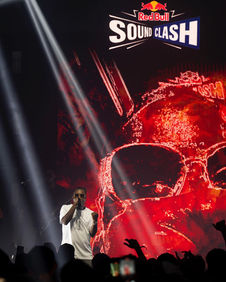 Un artiste sur scène avec des projections visuelles rouges dominantes en arrière-plan, renforçant l’énergie de la performance. Le logo RedBull Soundclash est bien en évidence, contribuant à l’identité visuelle de l’événement.