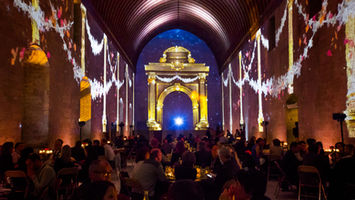 Invités dînant dans une ambiance immersive, entourés de projections de guirlandes lumineuses et d’arches dorées, évoquant l'époque historique du Palais des Papes.