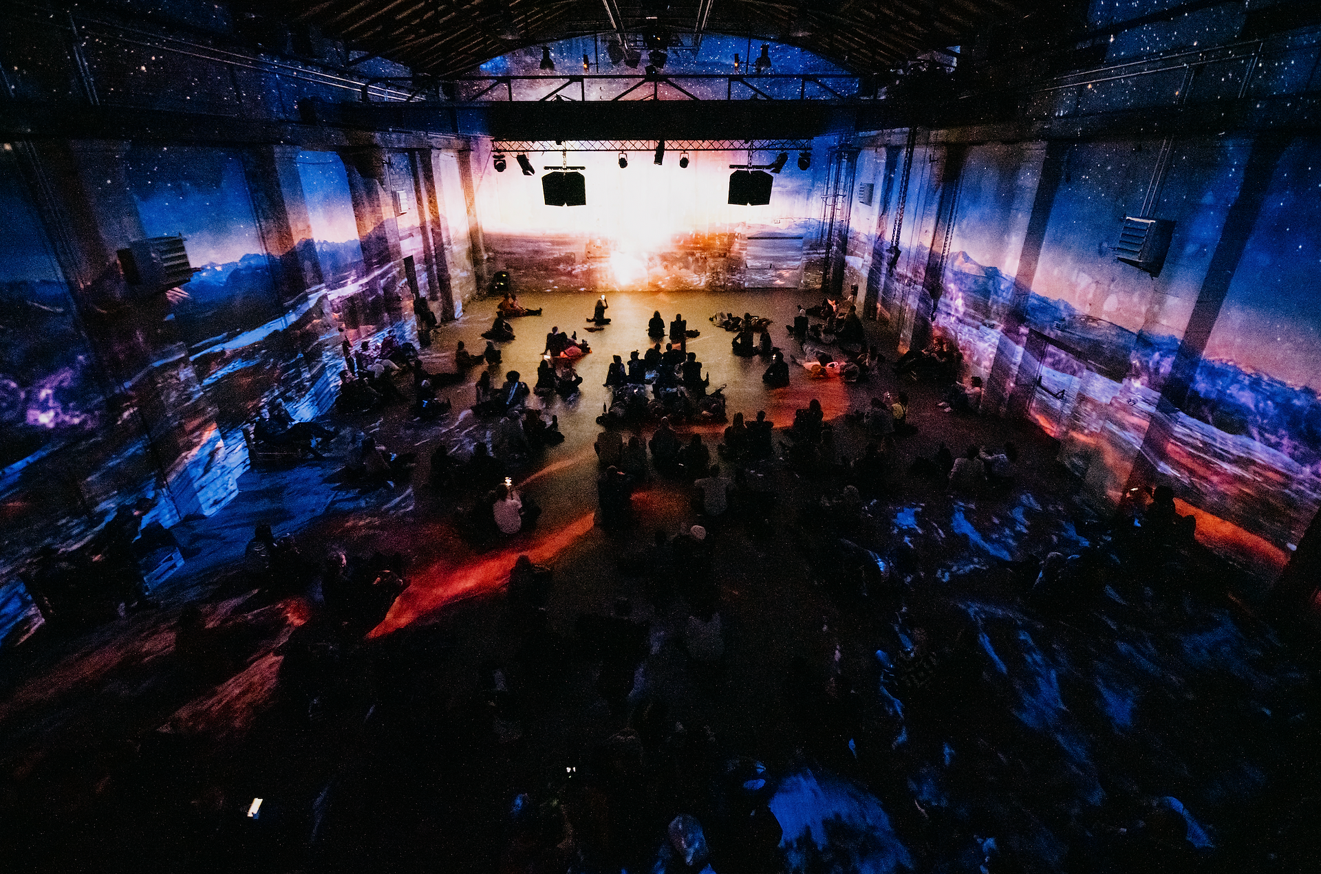 La même salle transformée par des projections panoramiques de paysages naturels et d'effets lumineux bleutés. L'ambiance devient onirique, avec un décor qui évoque des montagnes et un ciel étoilé, immergeant le public dans une atmosphère contemplative