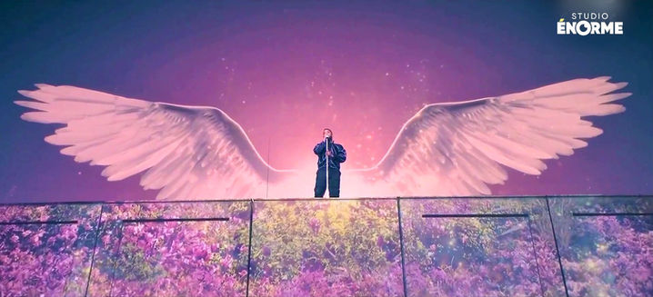 Slimane sur scène, avec de grandes ailes projetées en arrière-plan, créant une ambiance poétique et immersive pour cette chanson. L’utilisation de projections interactives a été un élément clé de la scénographie numérique.