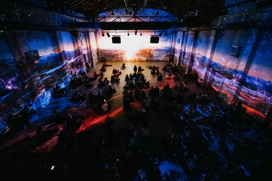 L'installation en cours de projection, montrant des visuels dynamiques enveloppant les murs et le sol, tandis que le public est assis en cercle, immergé dans l'expérience. Studio ENORME utilise des technologies avancées pour synchroniser les projections et la bande sonore, créant une expérience immersive puissante pour les visiteurs du Bright Festival 2023.