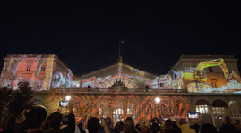 Animation dynamique projetée sur la façade, représentant des engins de chantier et des motifs géométriques lumineux, combinant modernité et patrimoine.