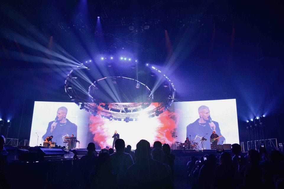 M Pokora sur scène devant un grand écran LED projetant des visuels spectaculaires, accompagnés de faisceaux lumineux créant une ambiance immersive pour le public. La scénographie numérique conçue par Studio Énorme amplifie la performance.