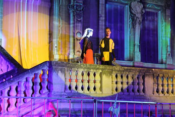 Acteurs en costume dans une scène colorée, avec des projections vibrantes en arrière-plan, donnant vie au Château Régis dans le cadre de la comédie musicale.
