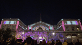 Éclairage artistique en tons violets et roses sur la même façade, créant une ambiance magique et féerique lors du spectacle nocturne.
