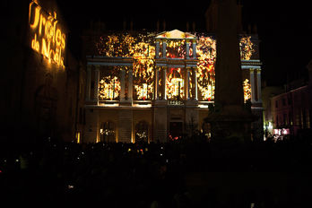 Spectacle de lumière dorée et festive sur la mairie d’Arles, captivant les spectateurs rassemblés en grand nombre.