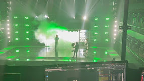 Sur scène, des effets visuels et des jeux de lumière créent une ambiance spectaculaire. Des membres de l'équipe de production ajustent les derniers détails pour capturer l'énergie électrisante de la performance rap à venir.