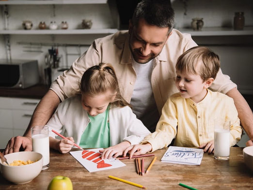 children with their father standing over them watching them draw Father's Day